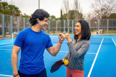 Young man and woman celebrating success with a fist bump, smiling and standing together on a bright