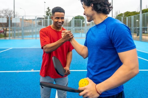 Two male pickleball players shaking hands on a blue outdoor court after a match, showing