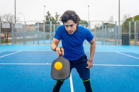 Young man in sportswear concentrating on a serve, gripping a pickleball paddle as a yellow ball