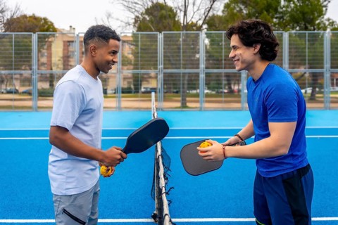 Two diverse young men standing on a vibrant blue pickleball court, holding paddles and balls,