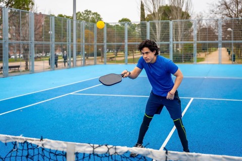Young man in blue activewear playing pickleball on a blue court, intently hitting a yellow ball
