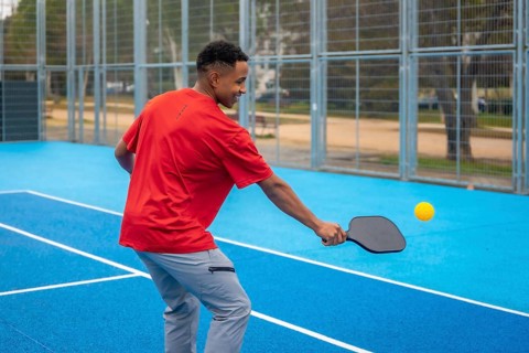 Young athletic man in sportswear striking a pickleball with a paddle on a vibrant blue outdoor