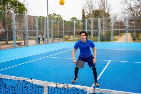 Young man actively playing pickleball on a vibrant blue outdoor court, holding a paddle and