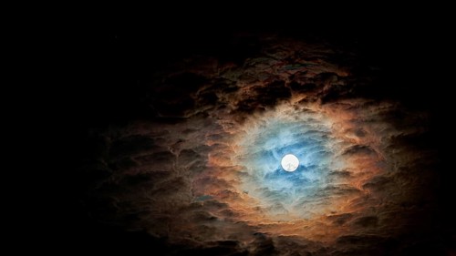Full moon surrounded by dramatic, colorful clouds in the night sky
