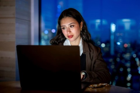 Young businesswoman focusing on her laptop screen, working late hours in a modern office