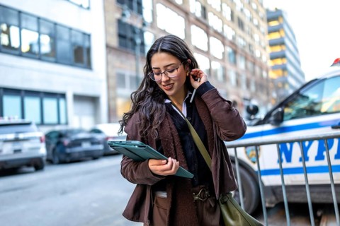 Young businesswoman in glasses walking manhattan streets, focused on her digital tablet while