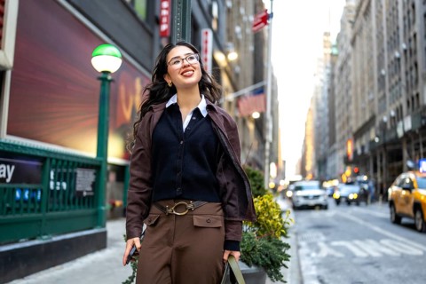 Young professional businesswoman smiling, walking confidently along a bustling street in manhattan,