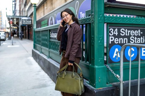 Young businesswoman in a brown jacket and glasses stands on a manhattan sidewalk near penn station,