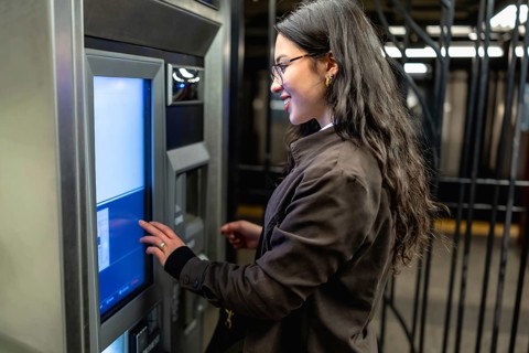 Young businesswoman standing at a subway station, operating an automated ticket machine to purchase