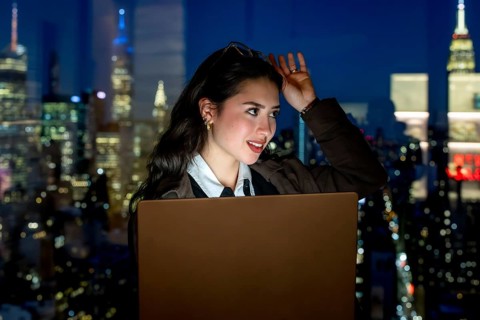 Young businesswoman working on laptop, thinking and looking away from a high rise office window at