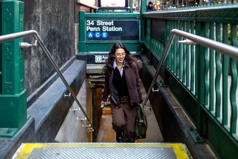 Young female executive with a satchel bag going down the stairs of the 34 street penn station a c e