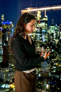 Young businesswoman standing by a window, engrossed in her smartphone, with the illuminated
