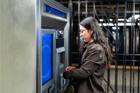 Young businesswoman with glasses and sleek dark hair interacting with a subway ticket machine,