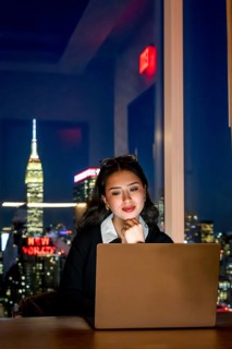 Young asian businesswoman focusing on her laptop screen, working late from an office with the