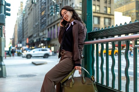 Young businesswoman smiling on a phone call, leaning against a green subway railing on a busy