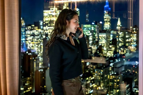 Young businesswoman in a high rise office talks on her phone at night, overlooking manhattan's