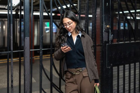 Young businesswoman with glasses checking her mobile phone while commuting in a manhattan subway