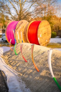 Colourful cables stick out of a snow hill, behind them colorful rolls of cable in winter light,