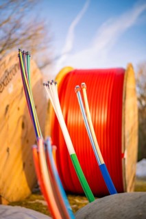 Colourful cables in a wintry environment in front of large, red cable spools, fibre-optic