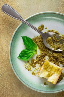 On a platter is a pesto sauce made from fresh basil, with a slice of bread and a spoon on a plate.