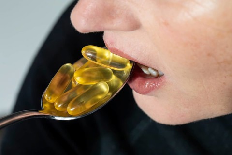 Face of a woman taking many omega capsules from a spoon