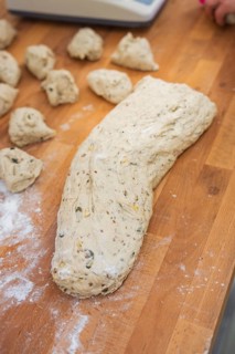 A large lump of dough and small pieces of dough on a floured wooden table, baking rolls,