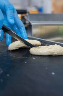 A person in gloves cuts dough with a knife in the bakery, baking rolls, Haselstaller Hof,