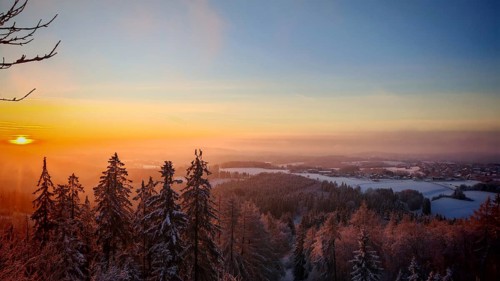 A wintry sunset over a snow-covered forest with glowing sky, Frankenwald nature park Park, Upper