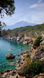 Rocky coast with clear blue water and view of snow-capped mountains in the background, view of