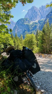 A bicycle on a dirt road in an alpine landscape with mountains and forests in the background,