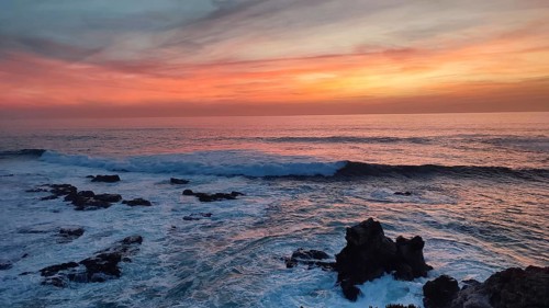 Dramatic sunset over the sea with waves crashing against black rocks, Southwest Alentejo Natural