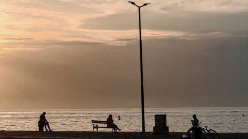 People sitting and bikers by the sea at sunset, quiet and peaceful atmosphere, waterfront, Izola,