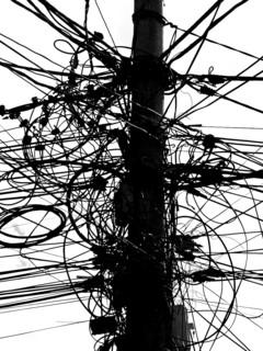 A power pole with a messy tangle of cables in an urban environment, black and white, Prizren,