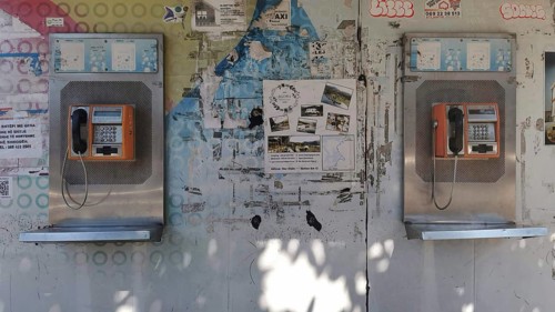 Two orange telephone boxes on a wall covered with graffiti and posters in an urban setting, Tirana,