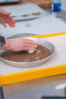 Hands press dough into a round dish filled with seeds on a yellow tray, bake rolls, Haselstaller