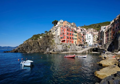 Colourful houses under blue sky, view of the fishing village of Riomaggiore, boats in the harbour,