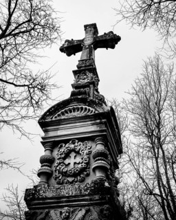 Gothic grave monument with cross in front of bare, wintery trees, black and white photograph, old