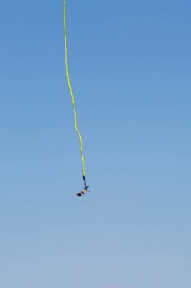 Female bungee jumper in midair with her ankles tied to a long yellow elastic bungee jumping cord,