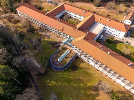A building complex with a red roof and a spacious courtyard with green space from a bird's eye
