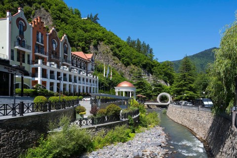 Hotel on a river surrounded by green mountains and vegetation in sunny weather, Hotel Crowne Plaza