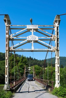 Car drives over an old suspension bridge surrounded by forest, camper, motorhome on a suspension