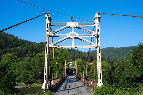 Steel bridge crosses a river amidst forested mountains, suspension bridge across the Kura River