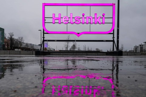 Large pink glowing city logo of Helsinki, in front of Oodi Central Library and Cultural Center,