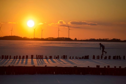 Ice skaters in front of sunset over icy landscape with wind turbines and intense colors on the