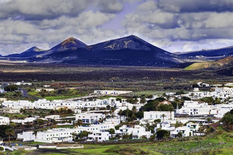 The municipality of Yaiza with white houses in a volcanic mountain landscape and cloudy sky, Yaiza