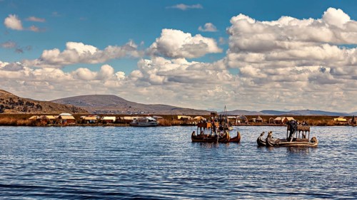 Traditional reed boats on a lake with a village on the shore under blue skies, The floating reed