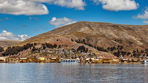 View of a lakeside village with hills in the background and clouds in the sky, The floating reed