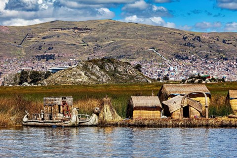 Reed houses and traditional lakeside boat under a cloudy sky with mountains, The floating reed