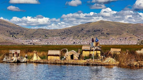 Reed huts and lakeside observation tower in sunny weather with mountains in the background, The
