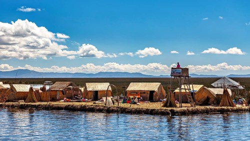 Reed huts and people on an island under a partly cloudy sky with a wide landscape, The floating